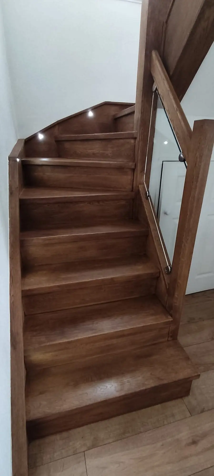 Oak staircase turning at the top, with a glass panel, timber newel and small step lights
