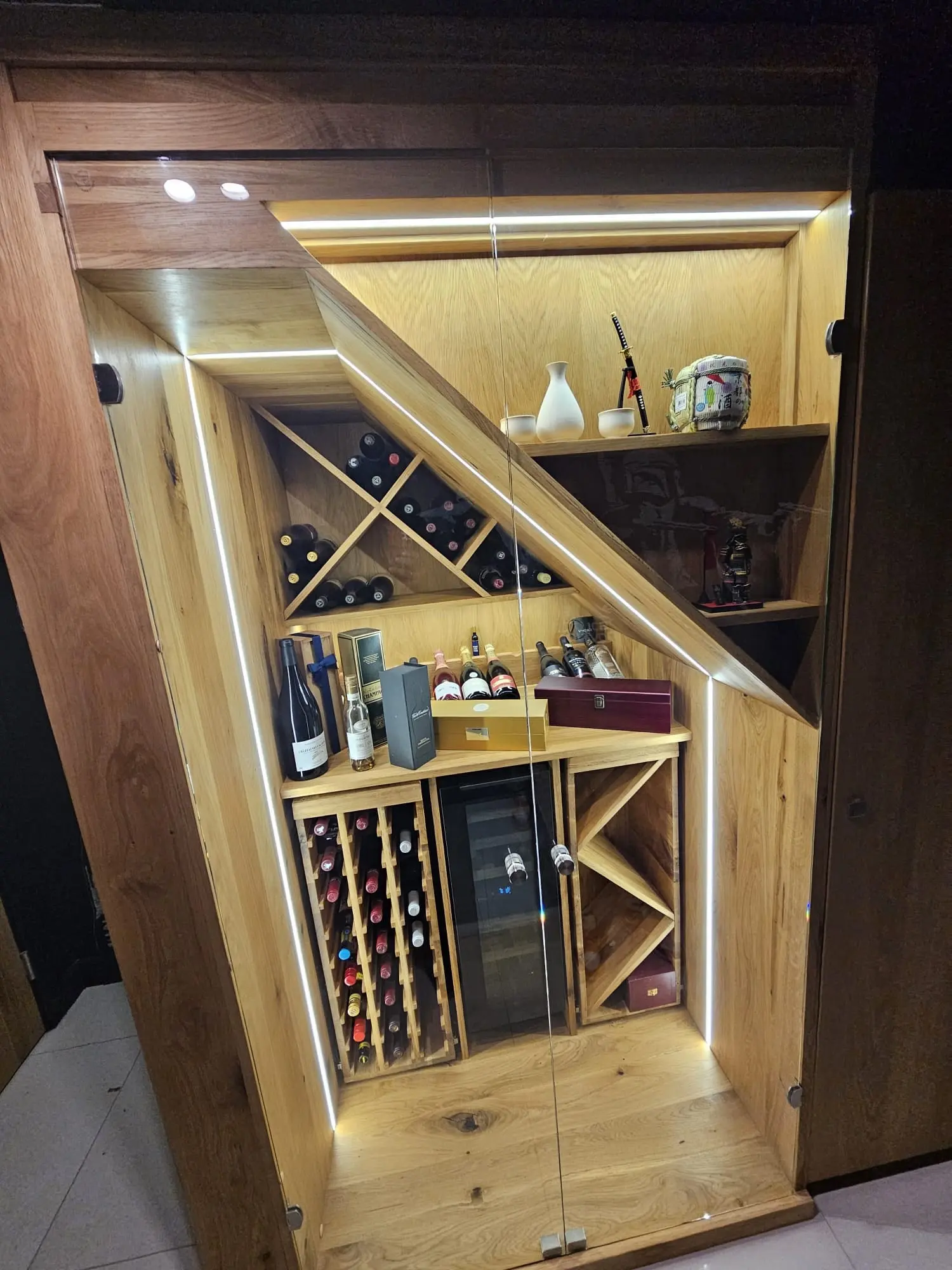 Corner view of a solid oak wine cabinet with an angled top, LED lighting and a glass door