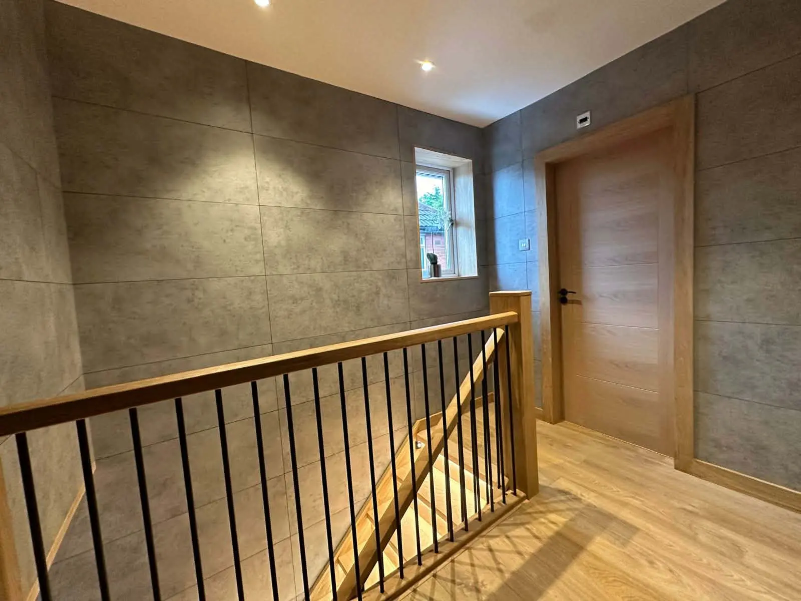 Landing with black vertical balusters, a timber handrail, a timber door and a textured grey wall